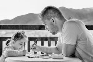 alt="a father helping his daughter write and draw on a balcony"