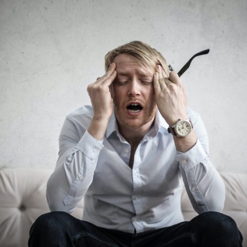 a man sitting in a sofa holding his temples in pain