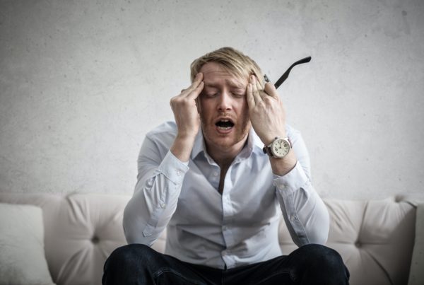 a man sitting in a sofa holding his temples in pain